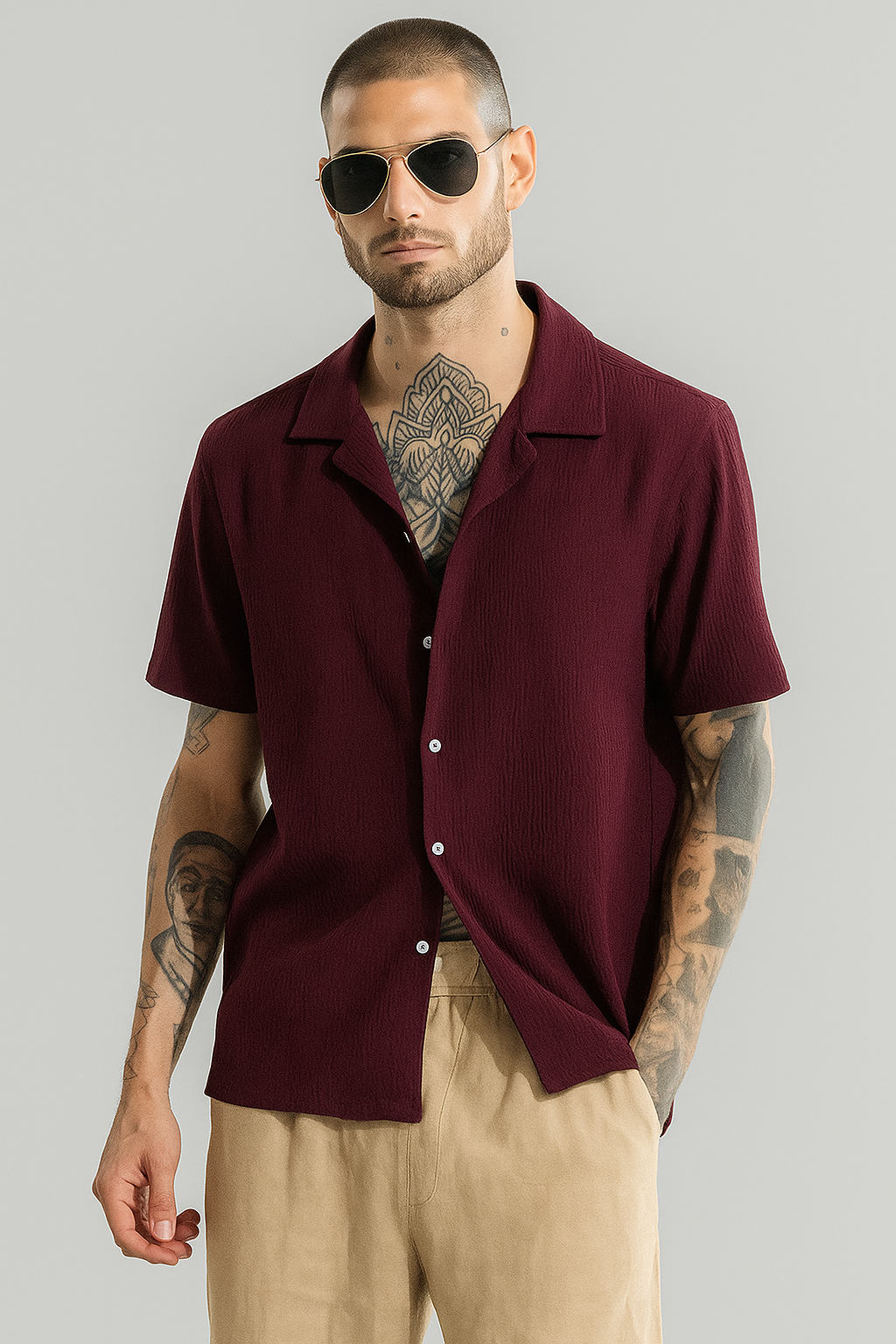 Man wearing a burgundy short-sleeve shirt and sunglasses against a gray background