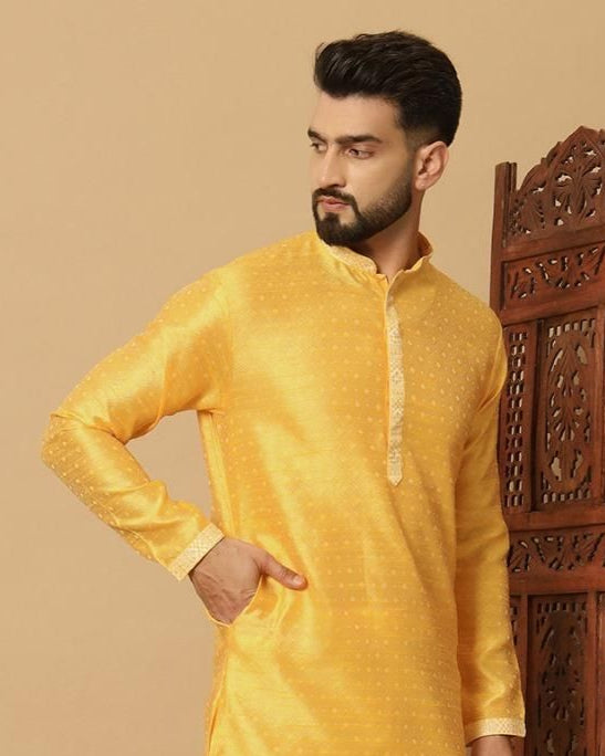 Man wearing a yellow kurta with white pants standing in front of a wooden carved screen.